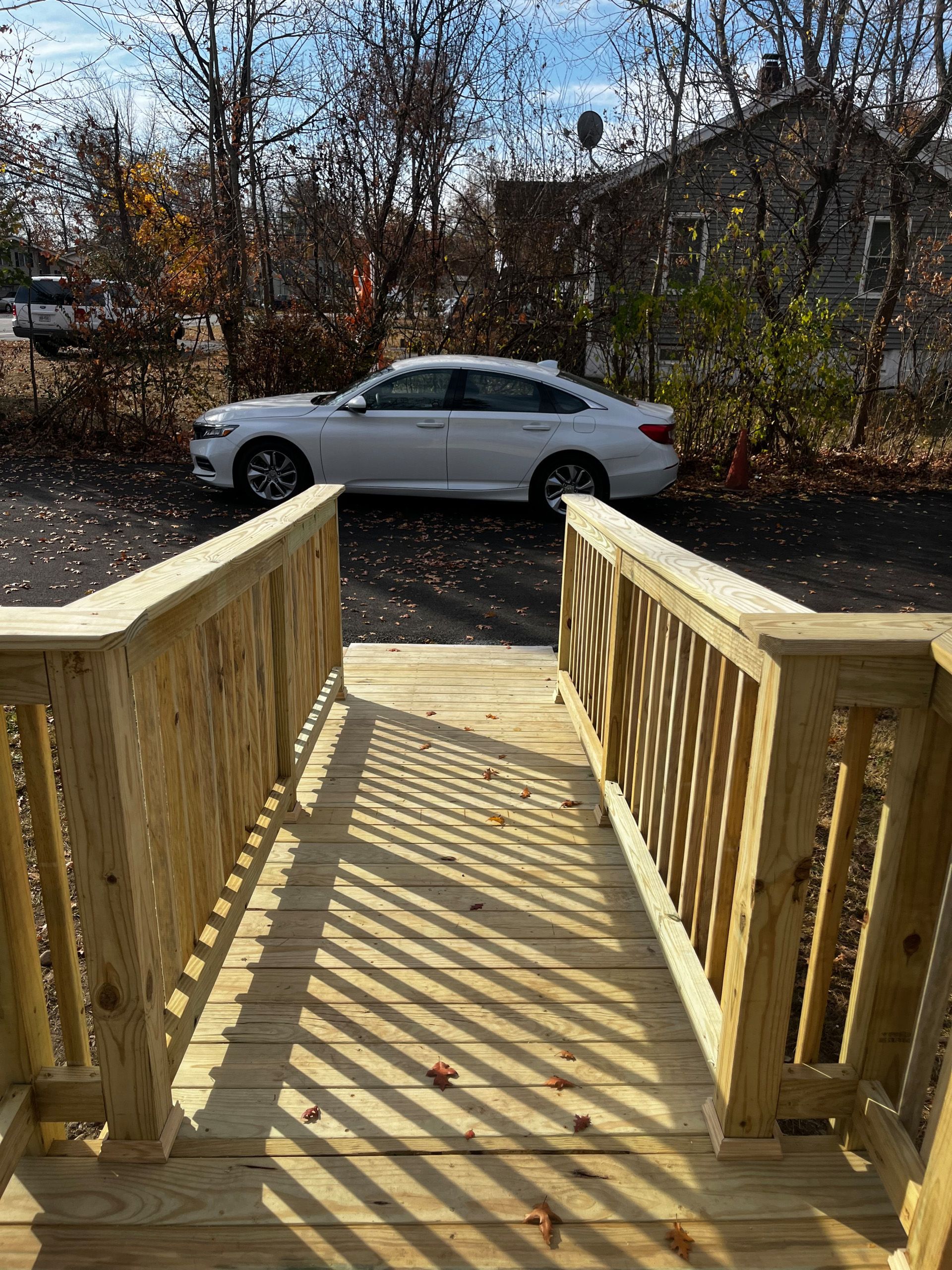Wooden stairs leading to a white car parked on asphalt, with bare trees and a building in the background.