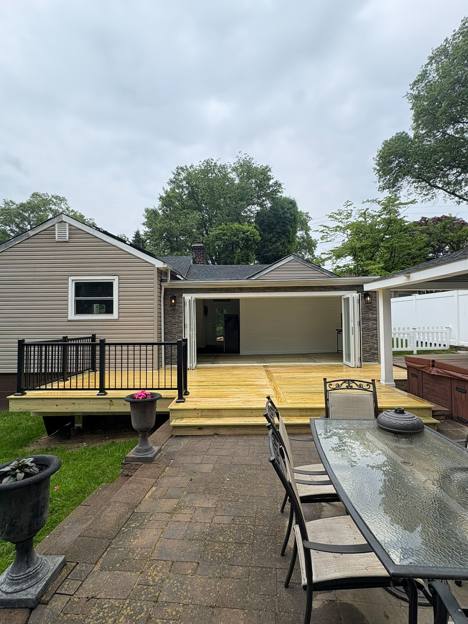 Backyard deck with a house, stone patio, and outdoor furniture.