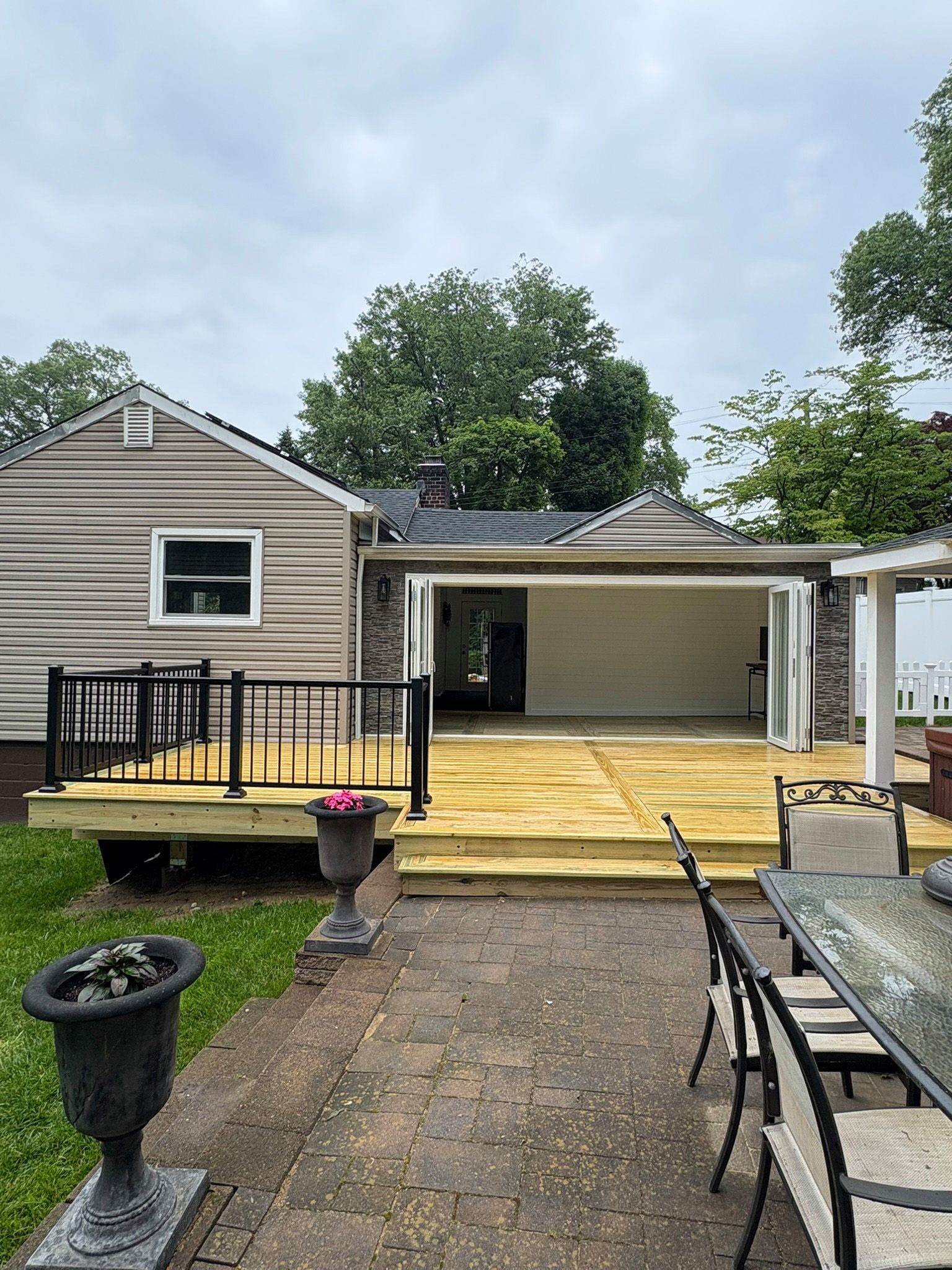 Backyard with newly built wooden deck, house with a partially enclosed patio and outdoor seating. Overcast.