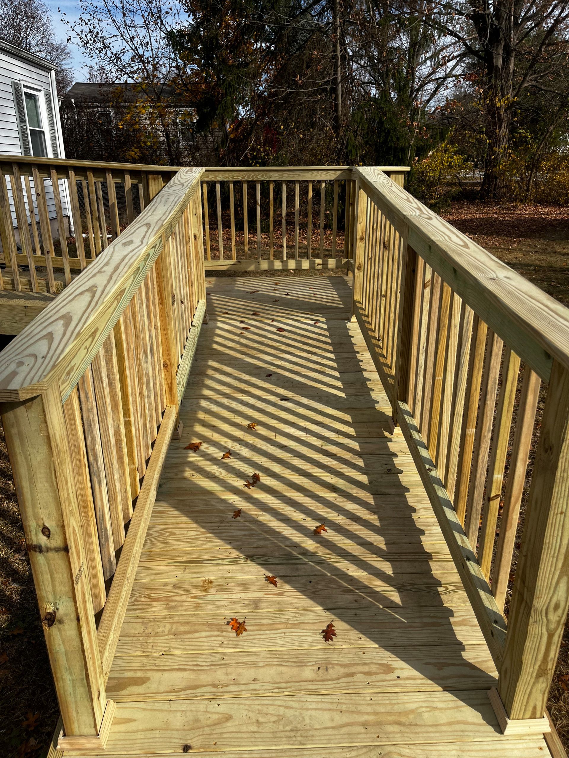 Wooden ramp with handrails leading to a house deck in an outdoor setting.