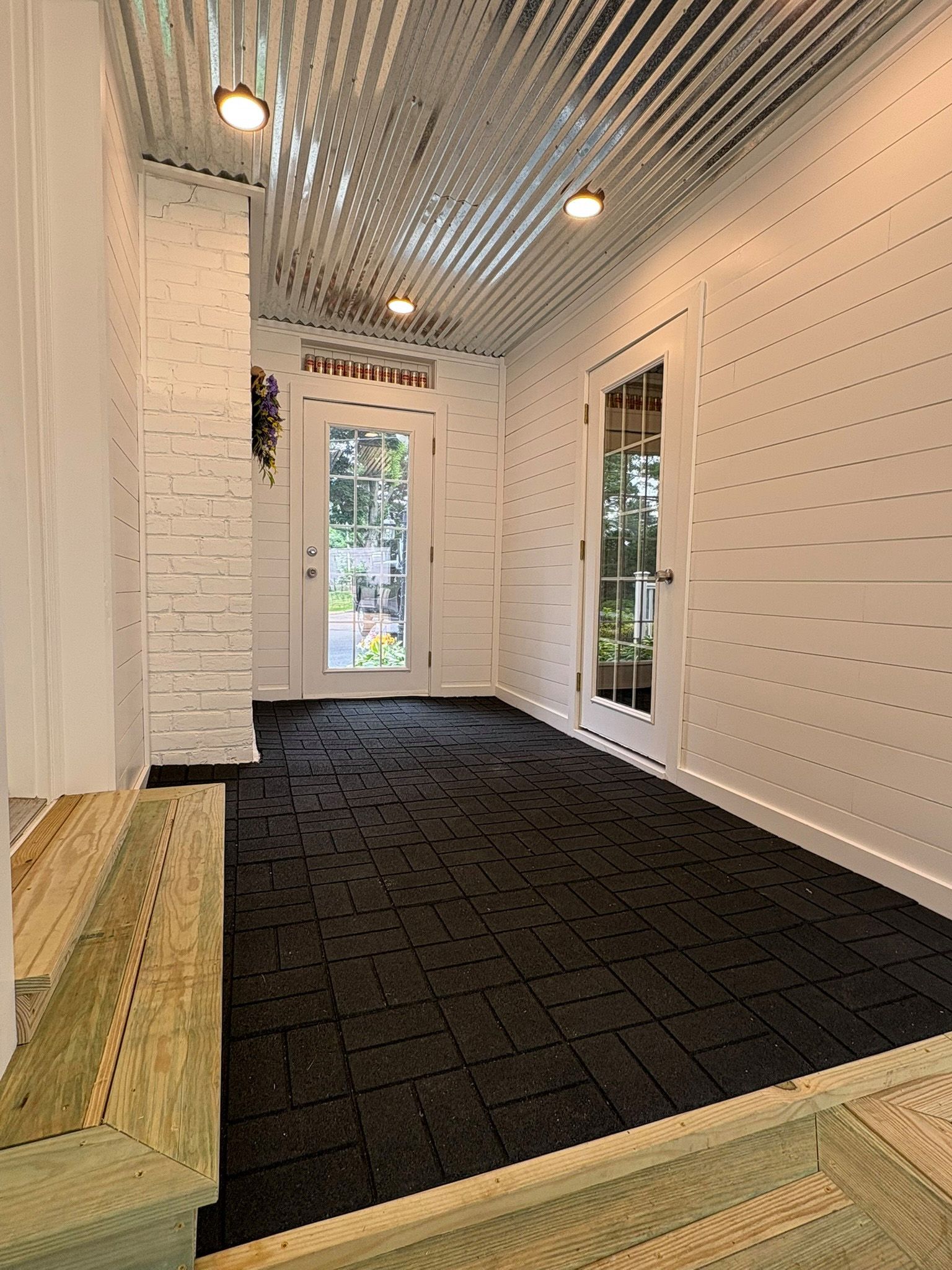 Narrow indoor space with dark floor, white walls, corrugated metal ceiling, and two glass doors.