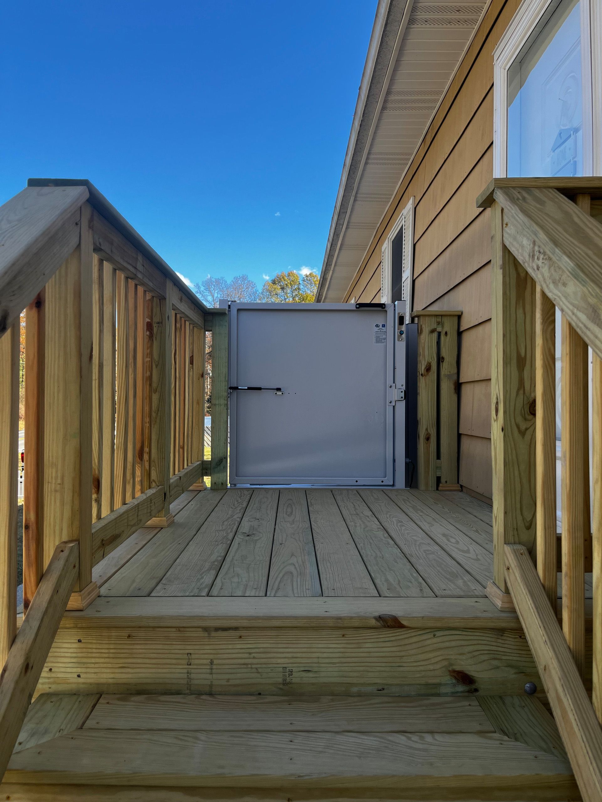Wooden deck with stairs, railing, and a metal gate leading to a door.