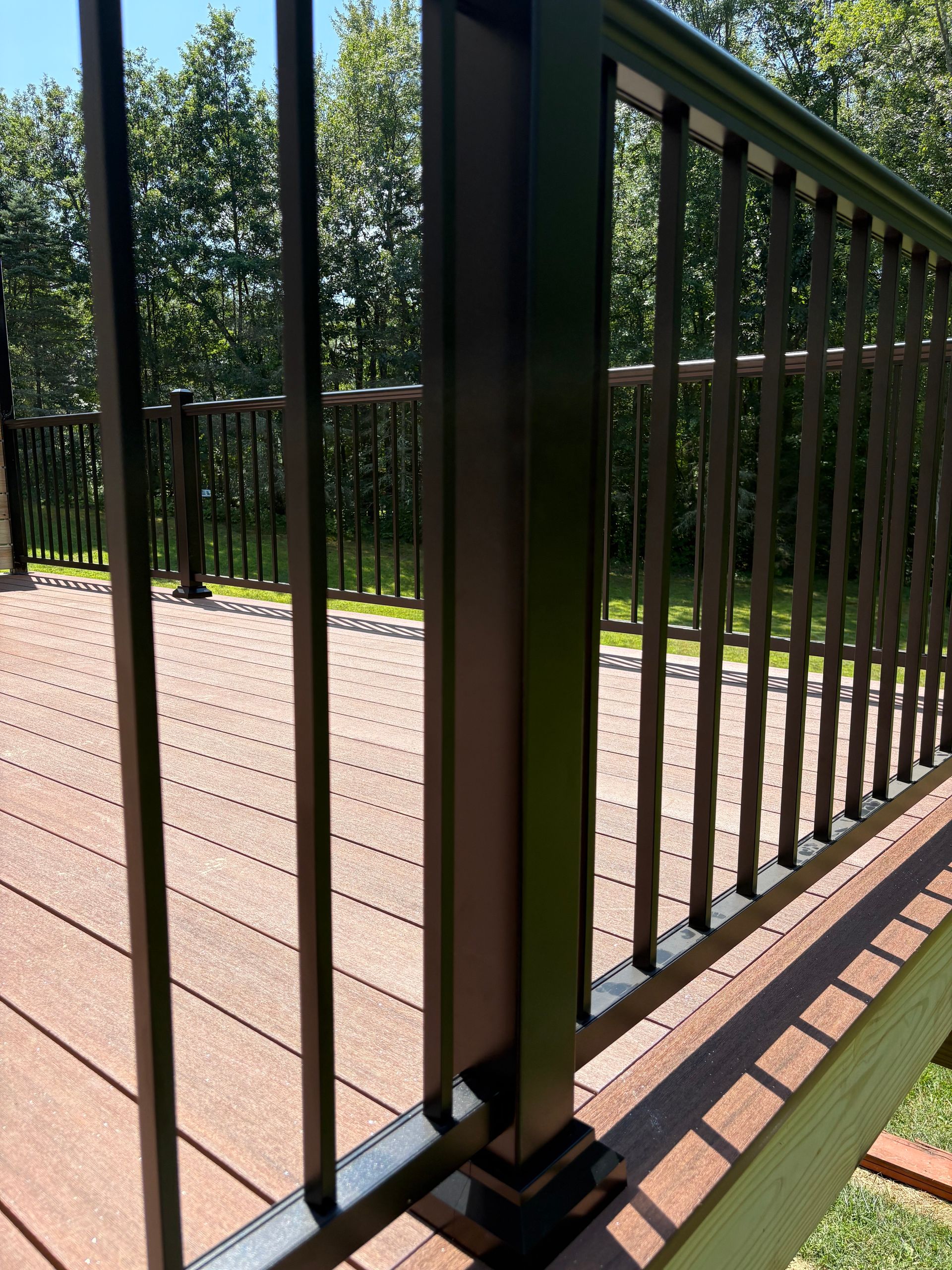 Brown composite deck with black railing in outdoor setting.