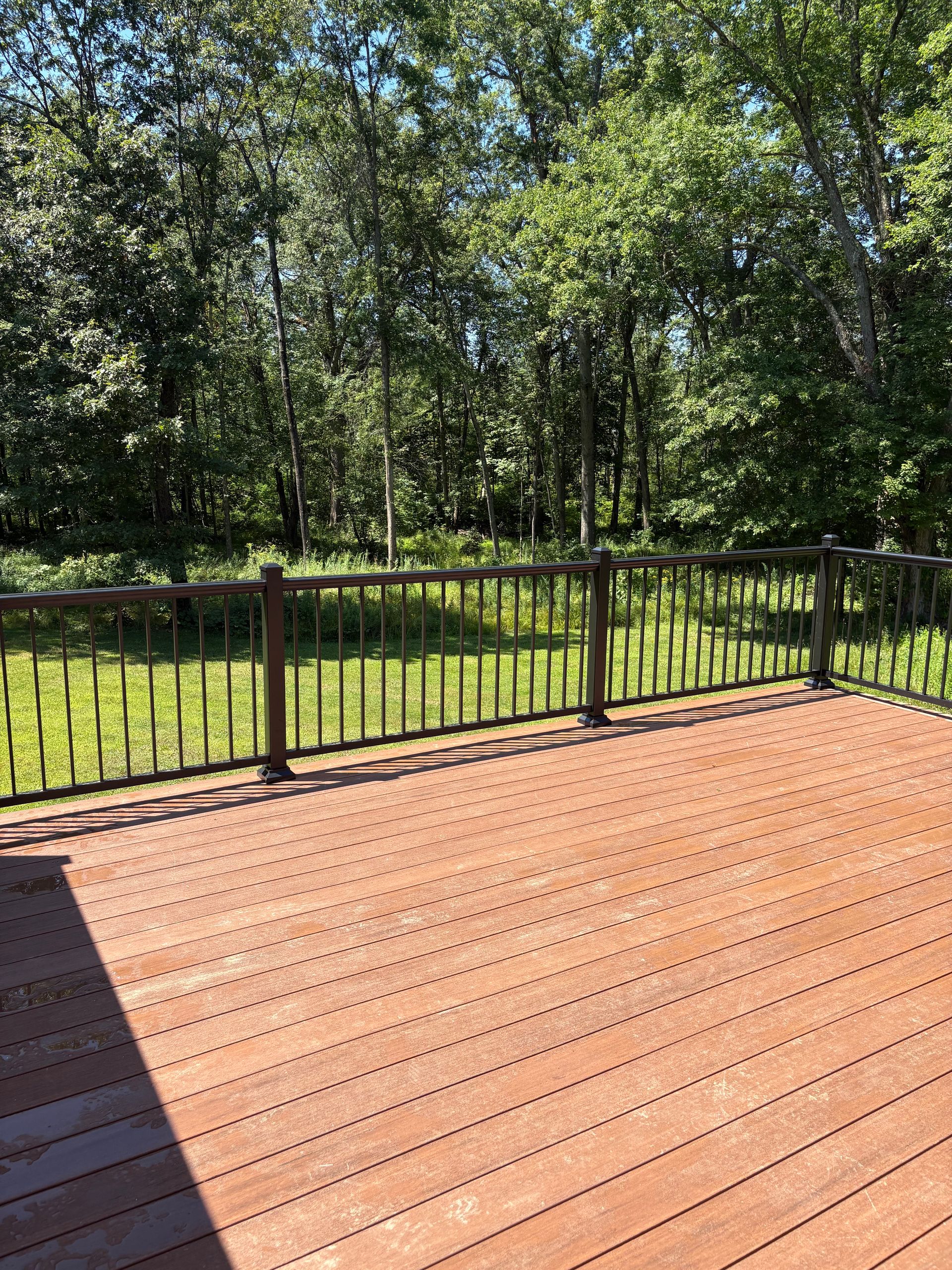 Wooden deck with dark railing overlooking a grassy area and trees.