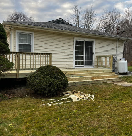 A light-colored house with a new wooden deck. A large propane tank sits to the right.