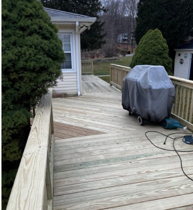 Wooden deck with a covered grill, surrounded by railings and trees.