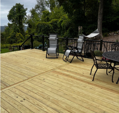 Wooden deck with black railing and furniture overlooking a green, wooded landscape.