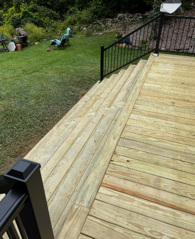 Wooden deck with steps leading to a grassy yard, black railing, and a recliner.