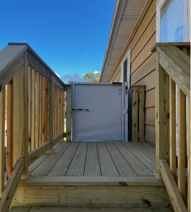 Wooden deck with ramp and metal door to home. Blue sky.
