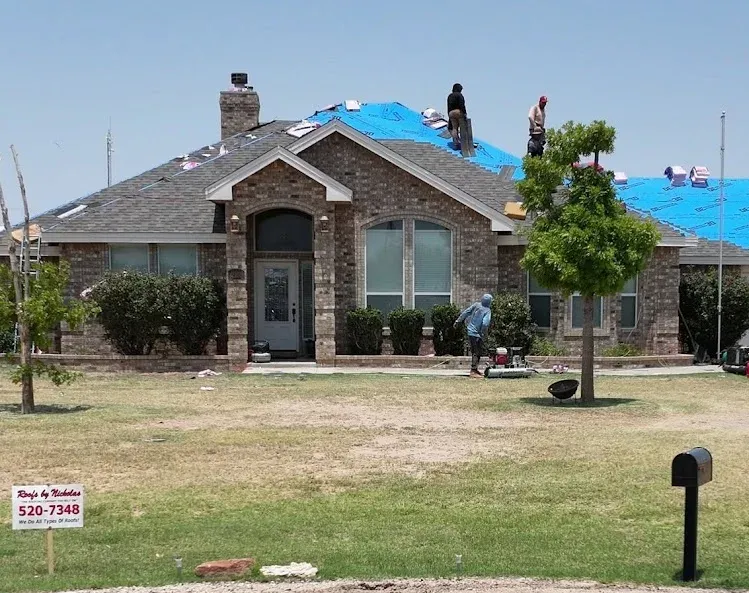 Roofs by Nicholas crew replacing the roof on a single-story brick home, with old shingles partly torn off and blue underlayment going down