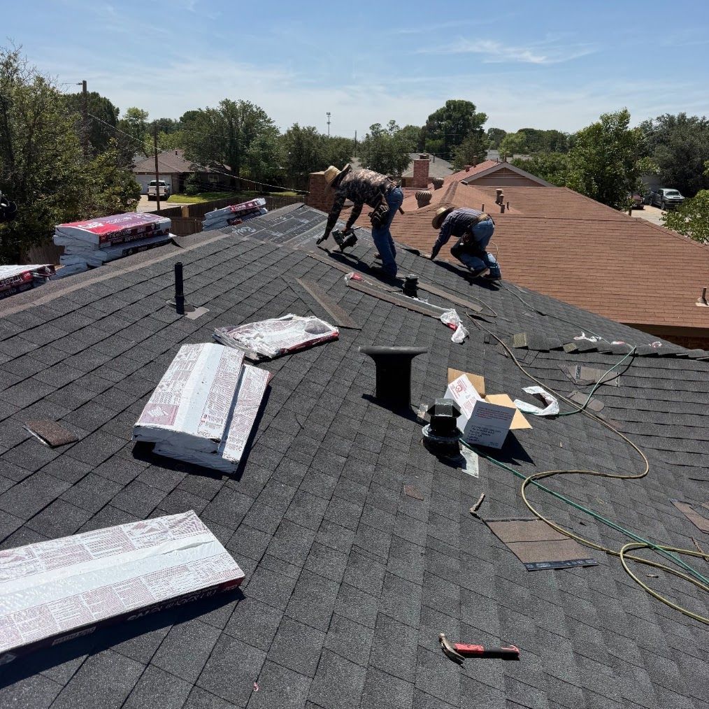 Roofing crew installing new black shingles with bundles staged on the roof