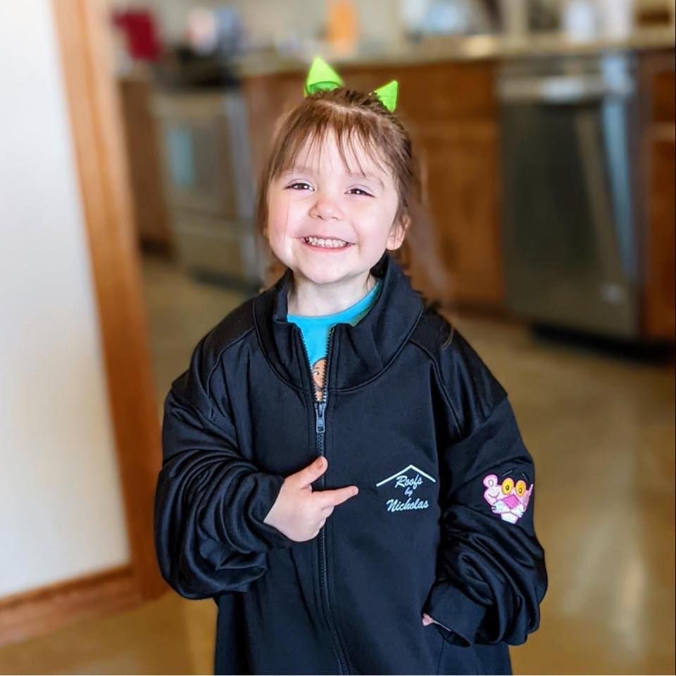Smiling young girl wearing a Roofs by Nicholas jacket and pointing at the logo
