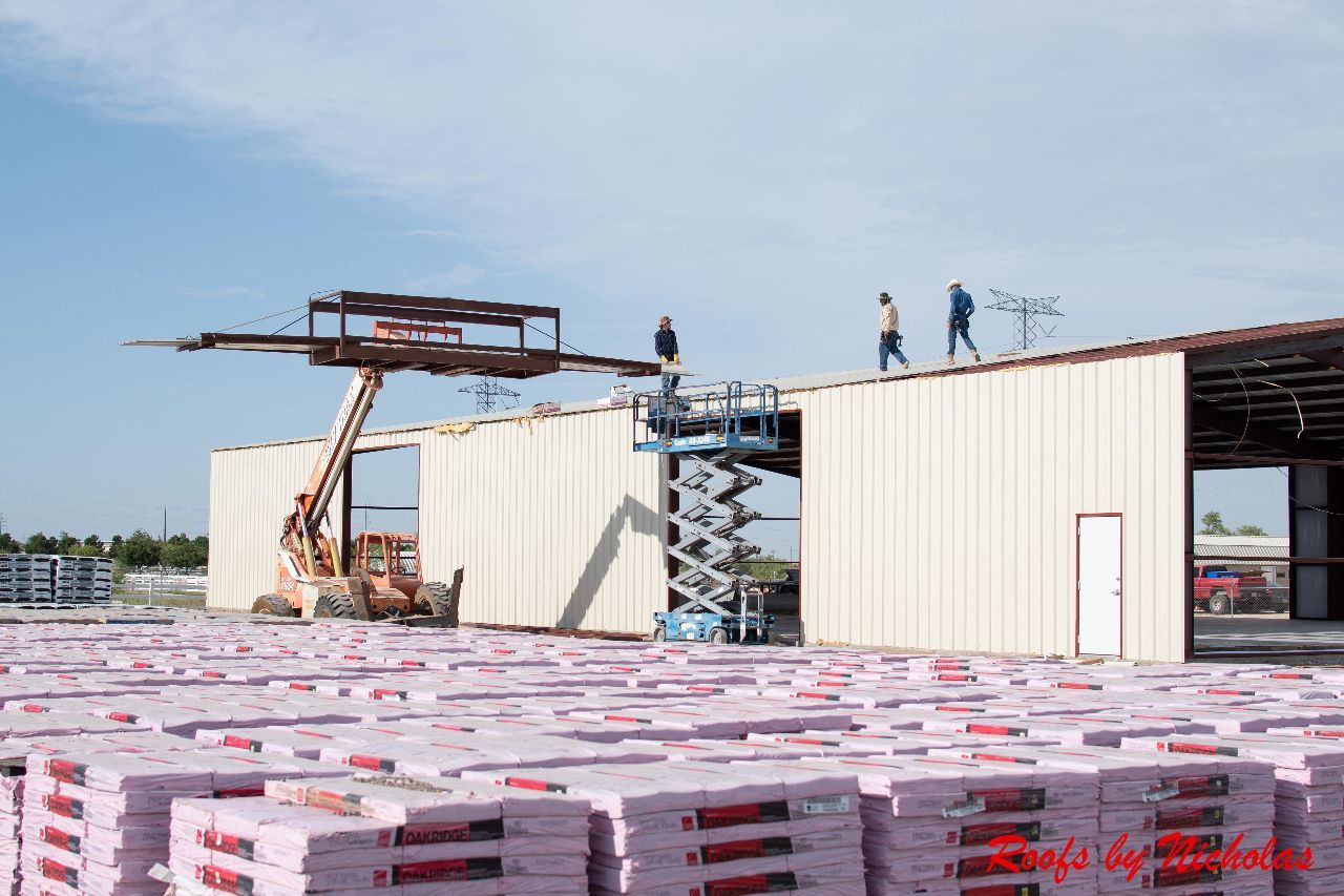 Construction crew working on metal building roof installation with lift equipment and roofing materials stacked onsite