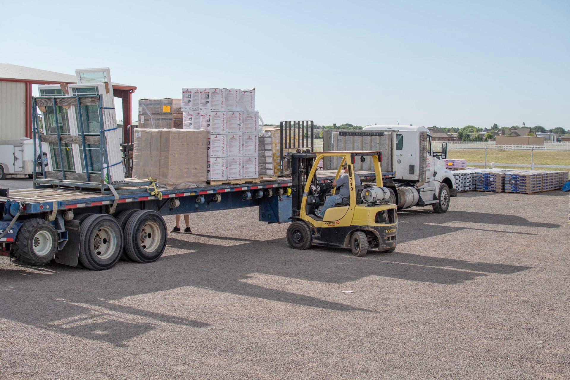 Forklift unloading roofing materials from flatbed delivery truck at Roofs by Nicholas yard