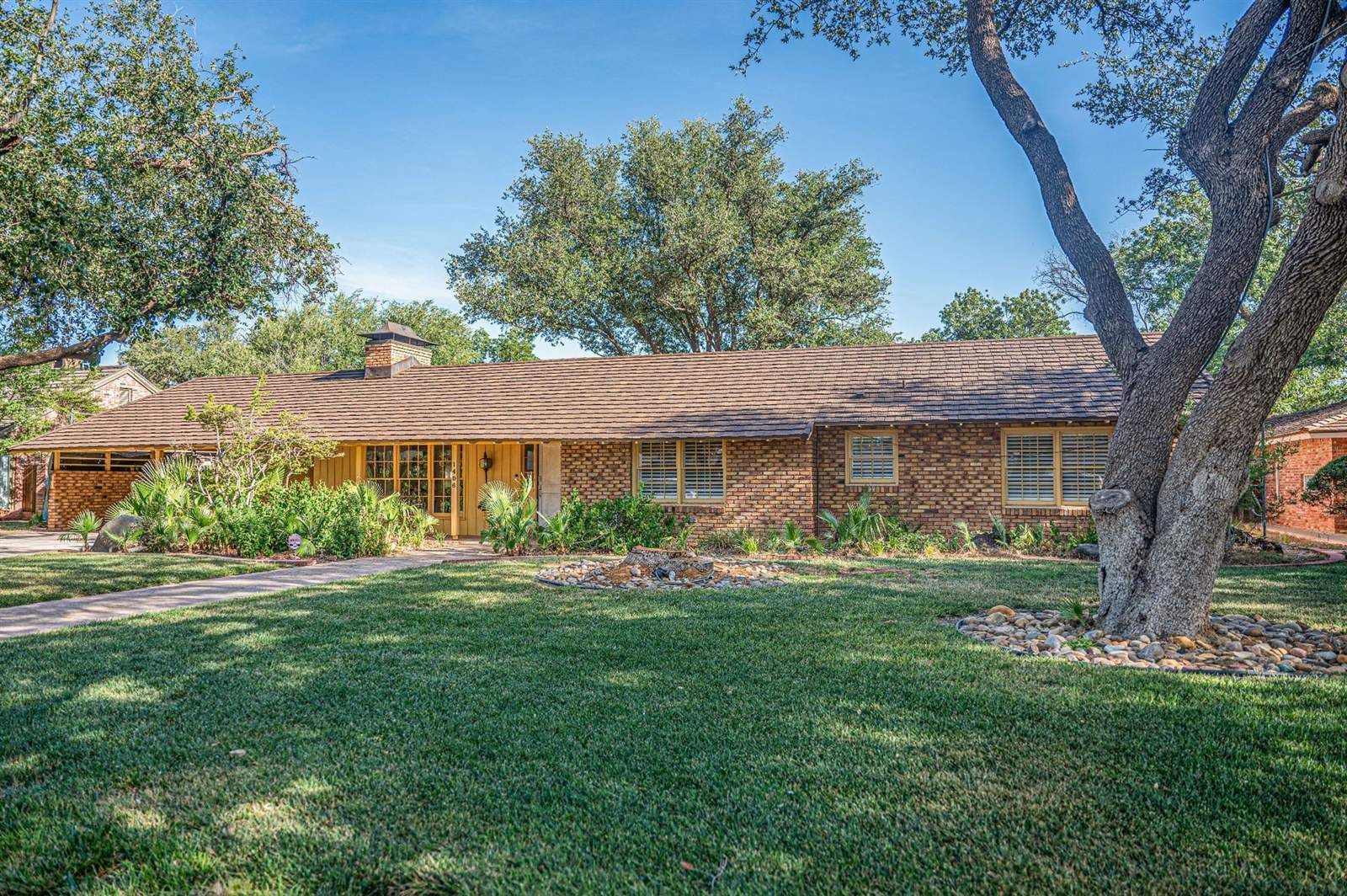 Brown shingle roof on a single-story brick ranch home with a landscaped front yard in West Texas