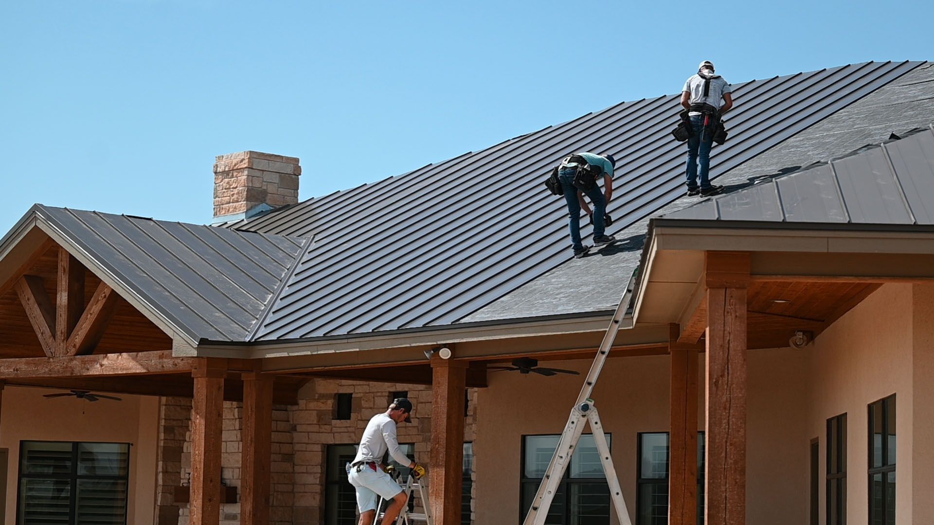 Roofers installing standing seam metal roofing on residential home