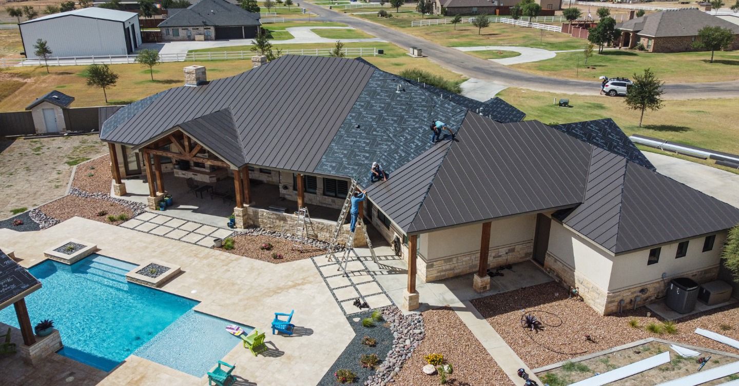 Aerial view of residential metal roof installation with crew working on standing seam panels