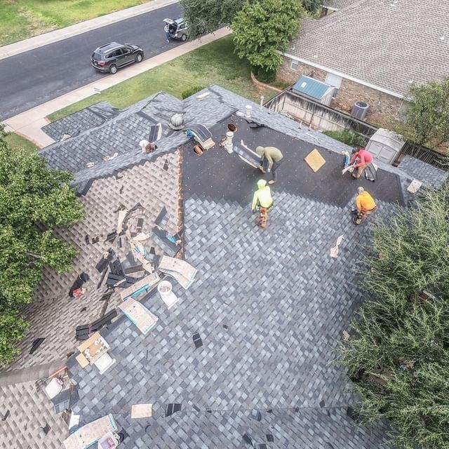 Roofing crew installing new grey asphalt shingles on residential roof