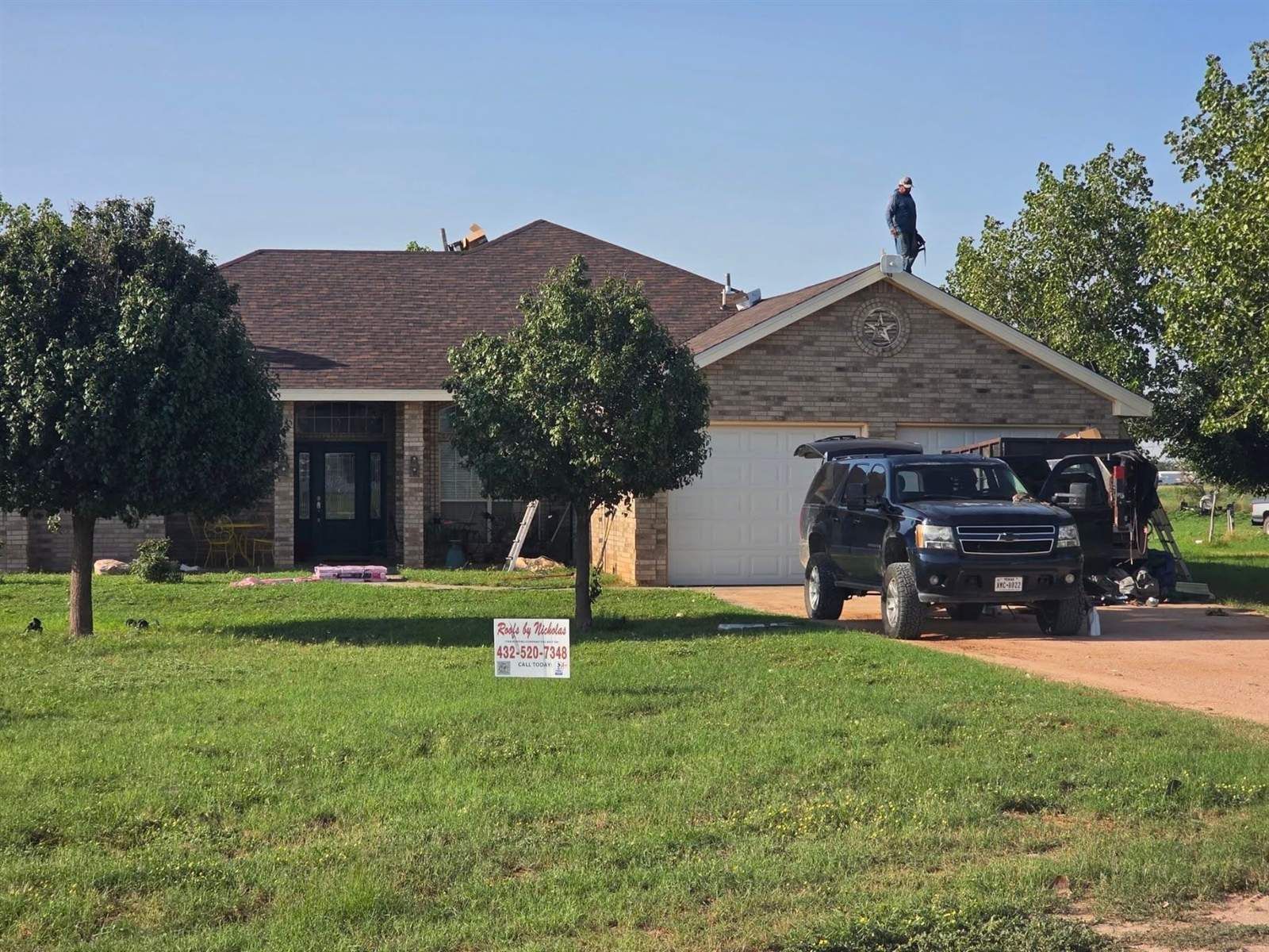 Roofs by Nicholas crew replacing the roof on a brick ranch home in West Texas, with a company yard sign in the front yard