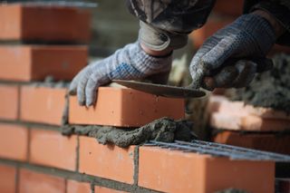 A man is laying bricks on a brick wall.