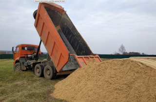 A dump truck is being loaded with dirt in a field.