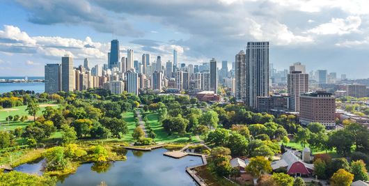 Chicago skyline with park and lake under a cloudy sky.
