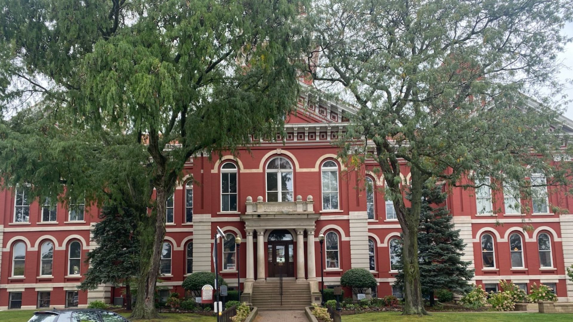Red brick courthouse, centered entrance, arched windows, and trees in front.