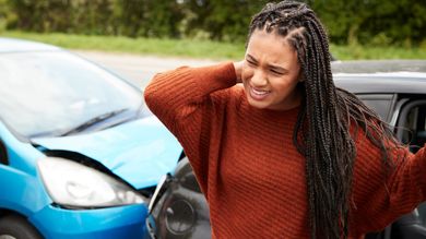 Woman holding neck in pain after a car accident. Cars with visible damage are in the background.