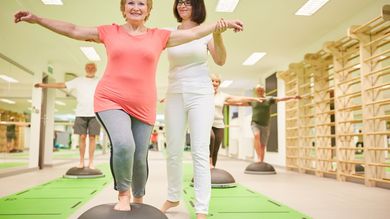 People balancing on exercise balls with an instructor in a gym setting.