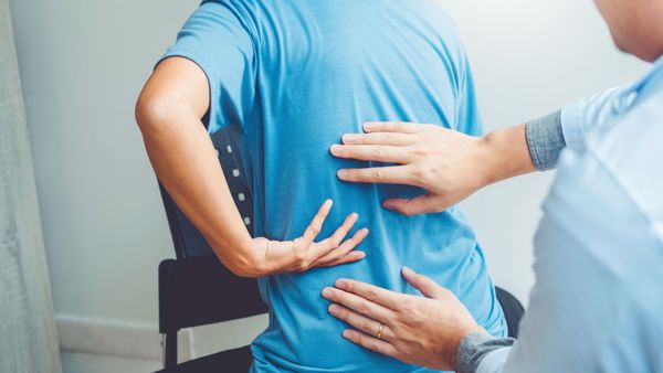 Person in blue shirt has back examined by healthcare professional.