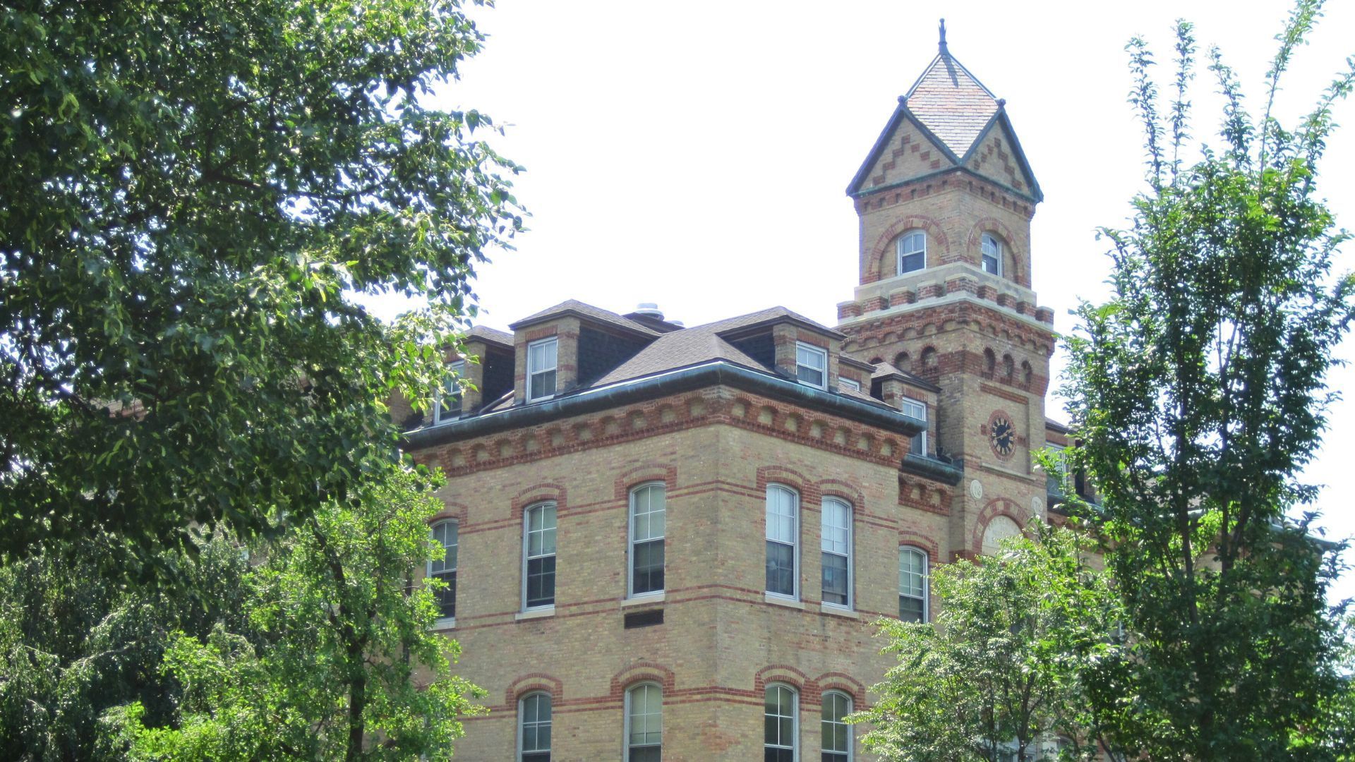 Brick building with tower, windows, and trees in the foreground.