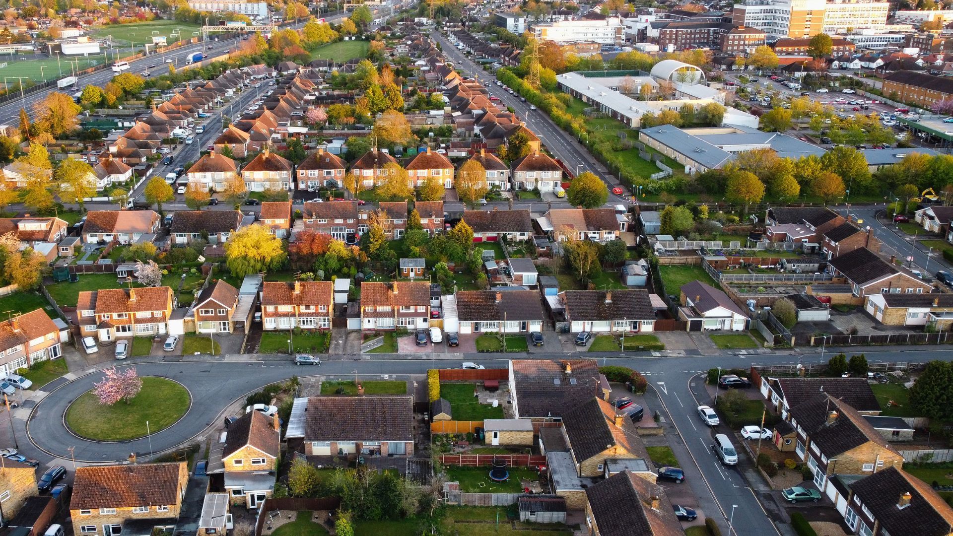 Aerial view of suburban houses with trees, roads, and a roundabout, bathed in warm sunlight.