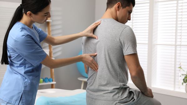 Physical therapist examining a patient's back in an examination room.