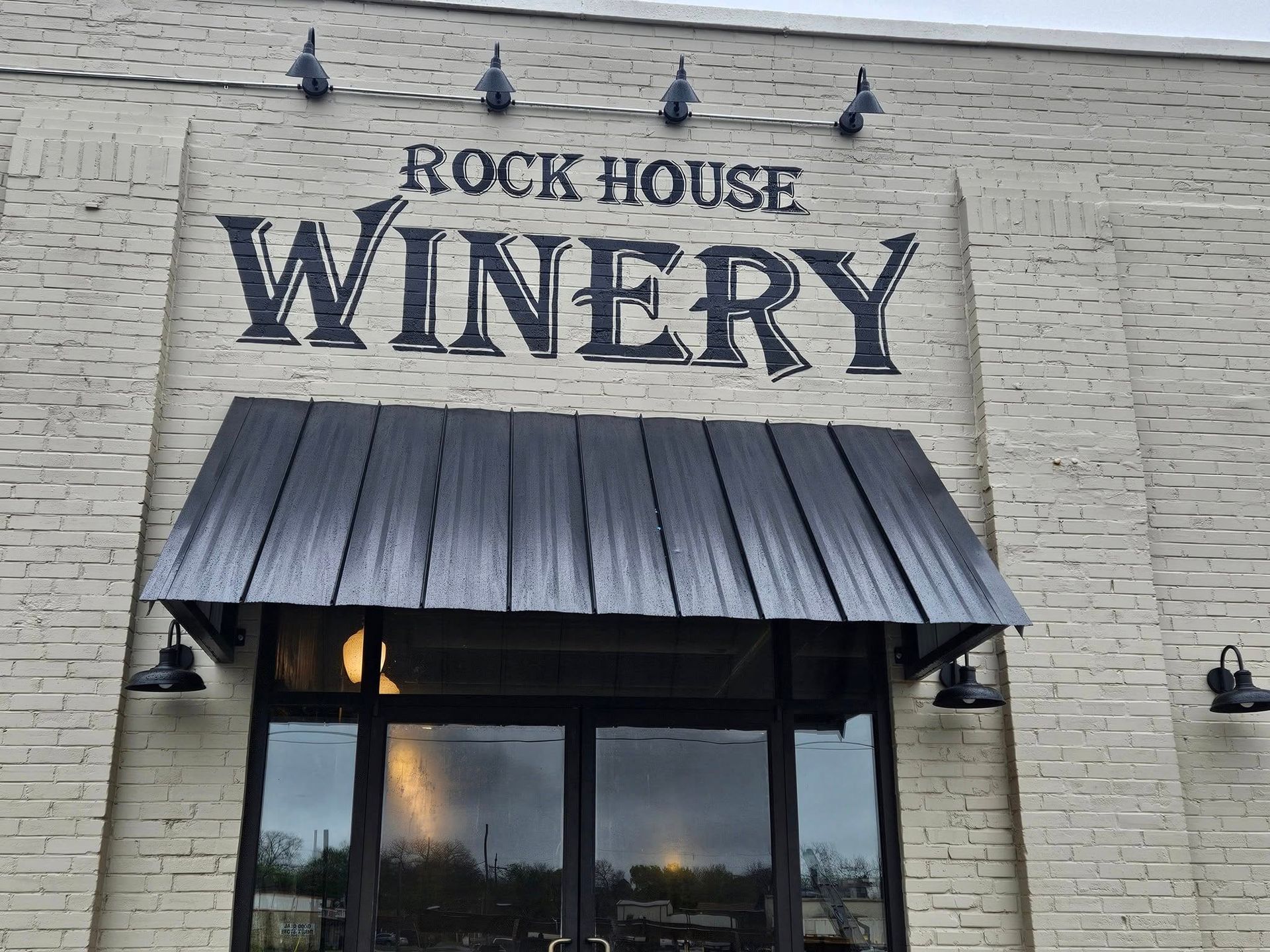 Rock House Winery exterior with black lettering on a light brick building, awning, and glass doors.