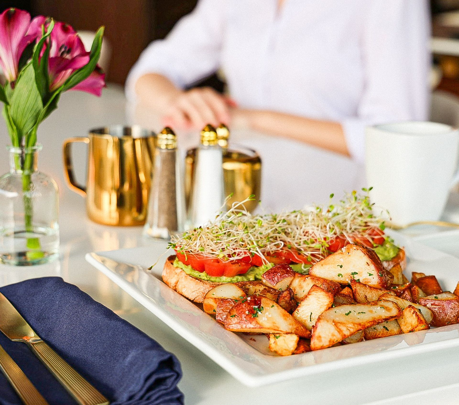 Bruschetta with potato wedges on a white plate, served at a cafe with a person blurred in the background.
