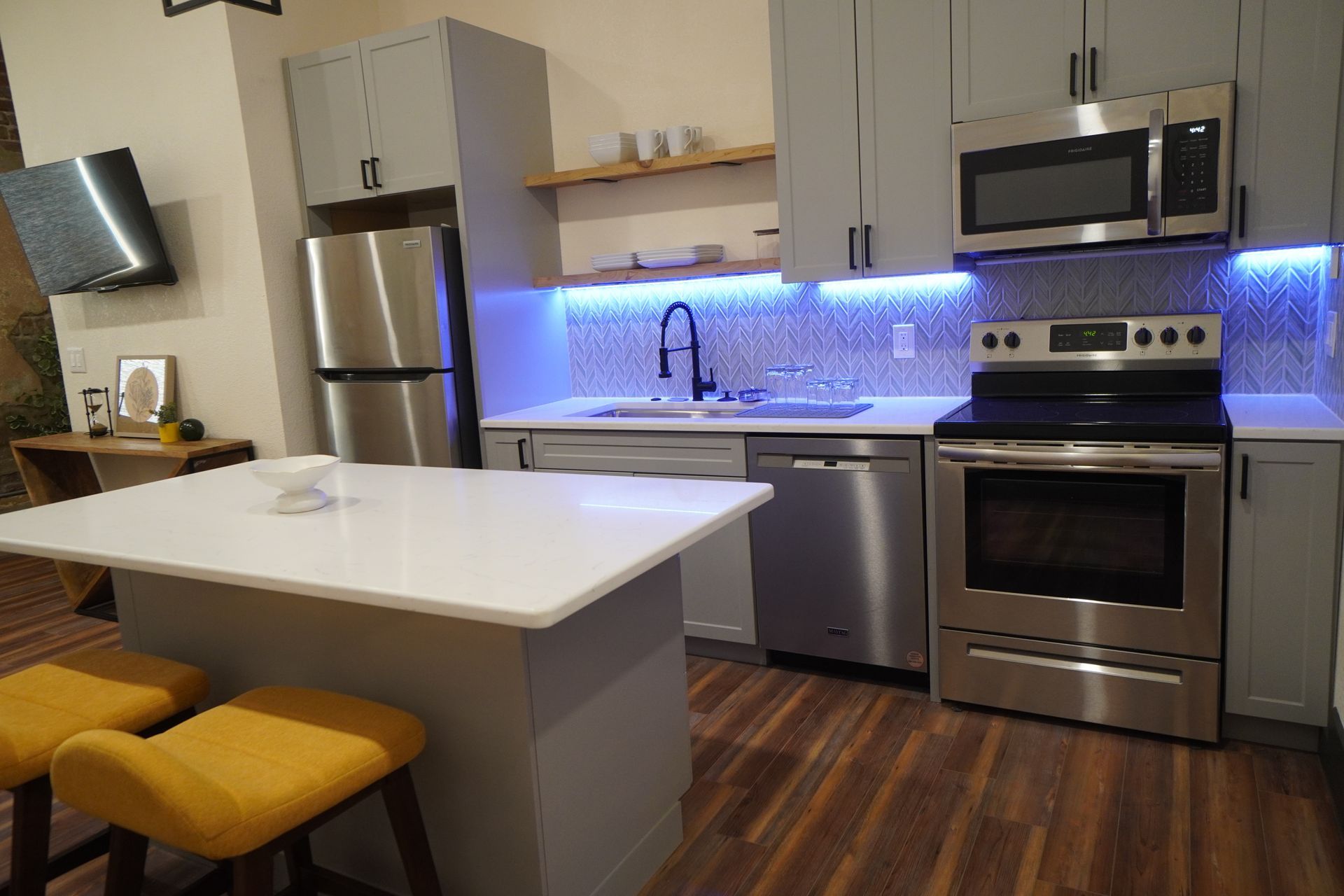 Modern kitchen with gray cabinets, stainless steel appliances, white countertop island, and wood flooring.