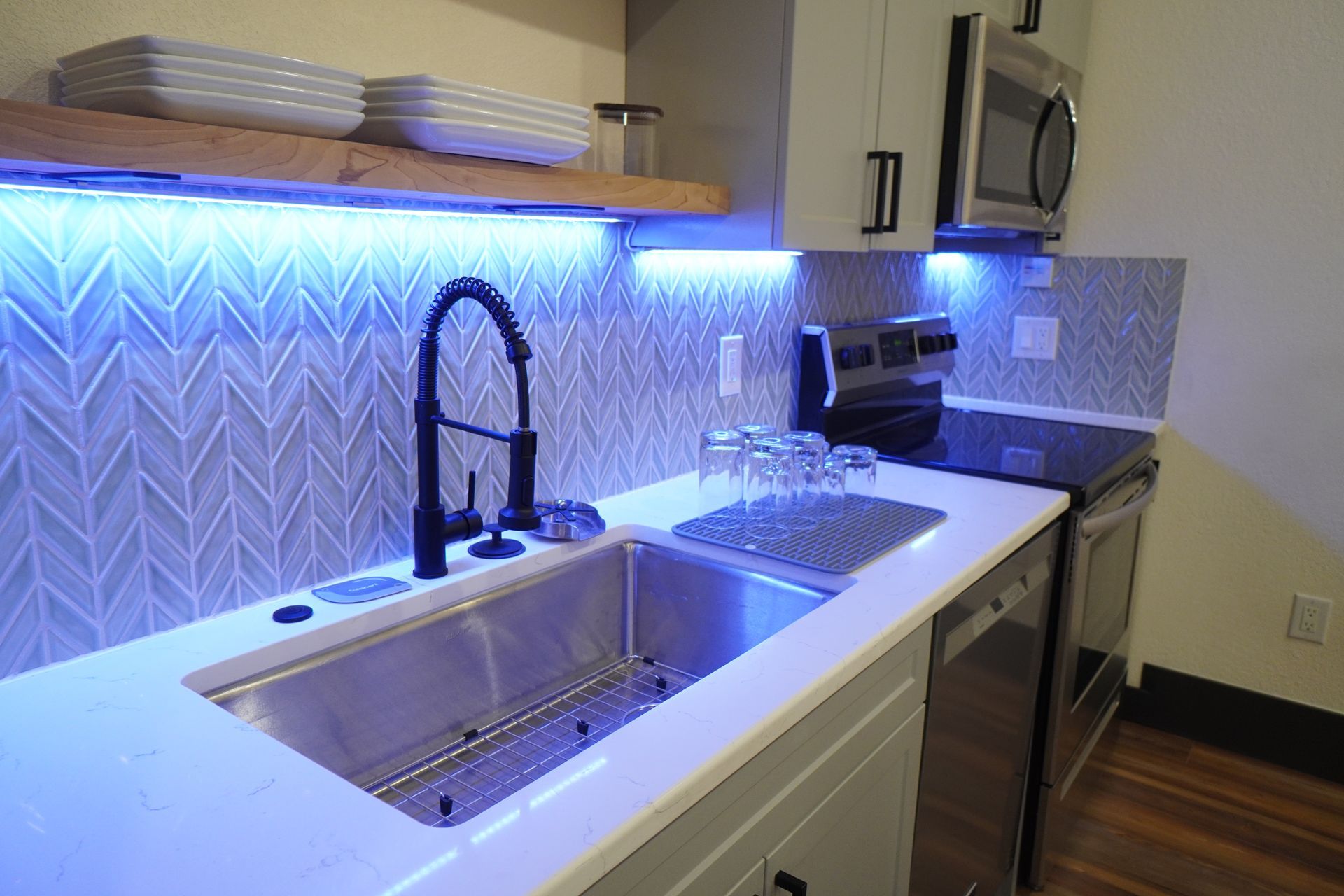 Modern kitchen with blue under-cabinet lighting, stainless steel sink, and light gray cabinets.