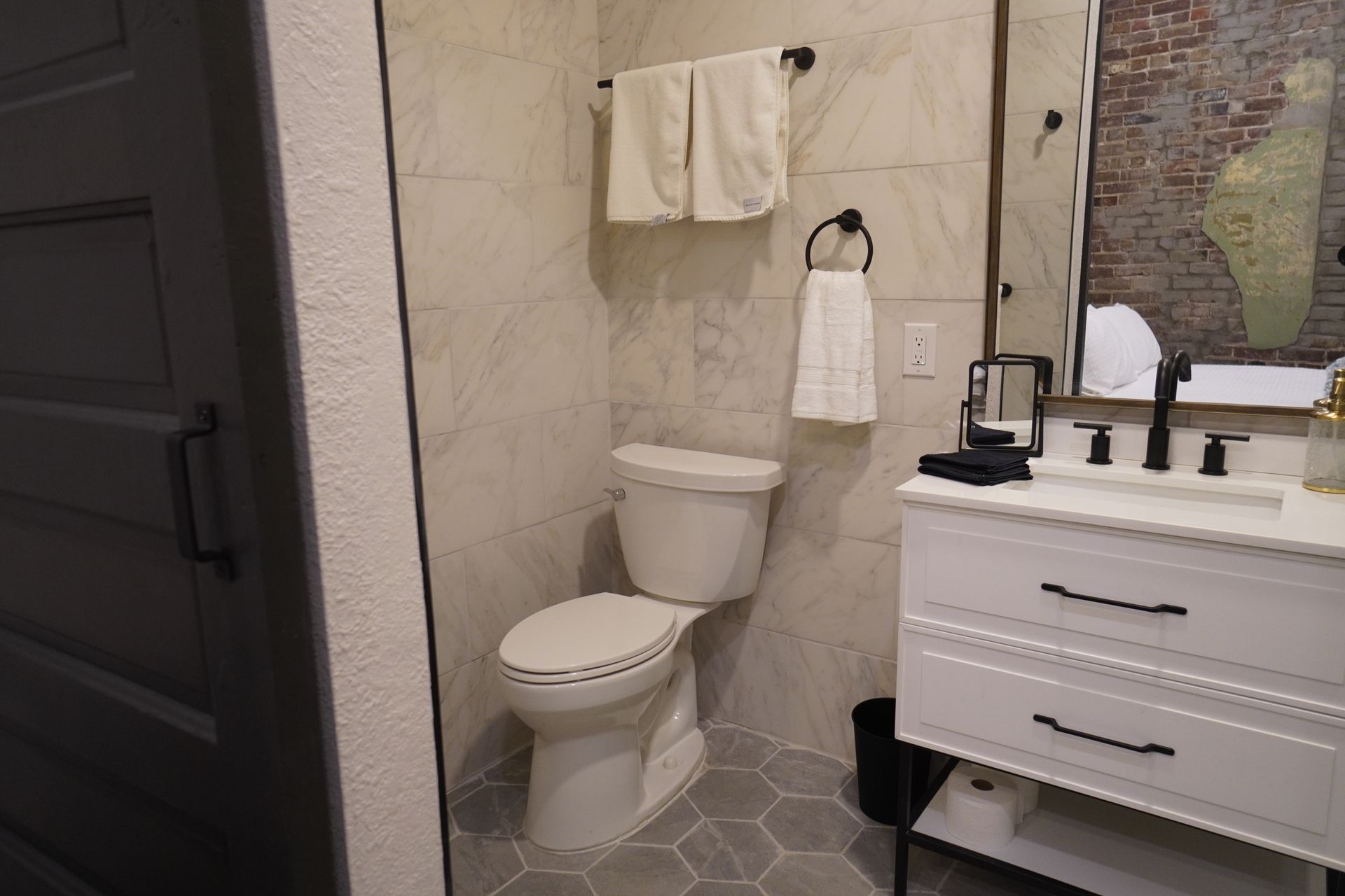 Bathroom with toilet, white vanity, and towel rack on tile wall; a partial view of door.