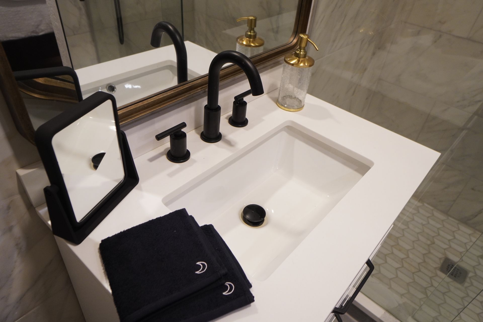 Modern bathroom vanity with a white countertop, black fixtures, and black towels.