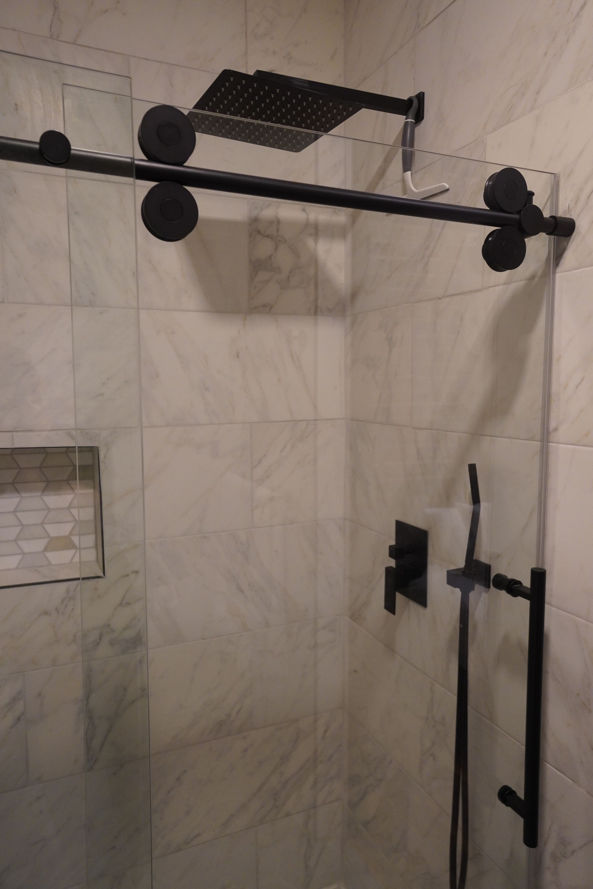 Black shower door with black fixtures on tiled wall.