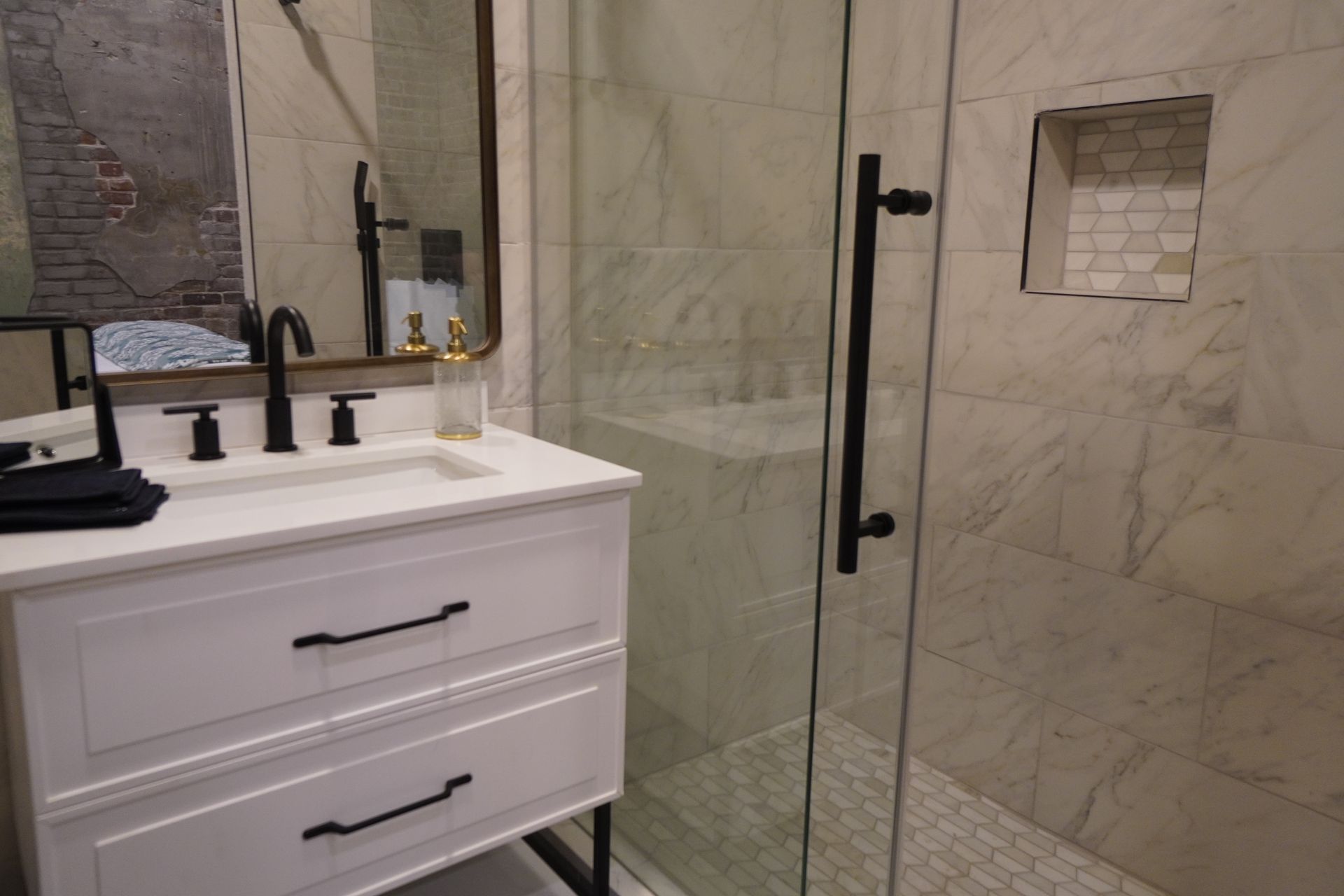 Modern bathroom with white vanity, black hardware, glass shower, and marble tile.