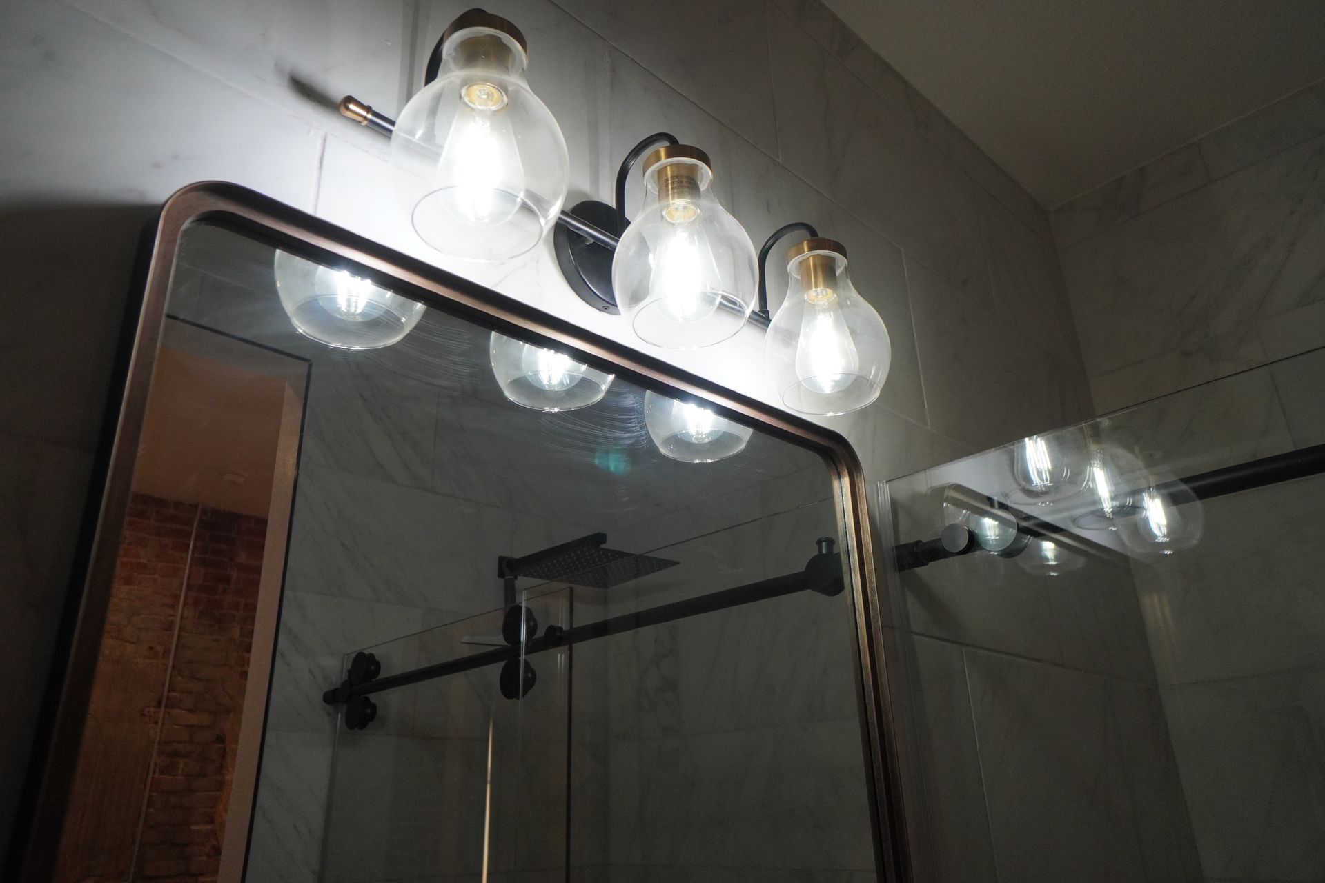 Bathroom mirror with copper frame and three-light fixture above it; a second mirror is reflected.
