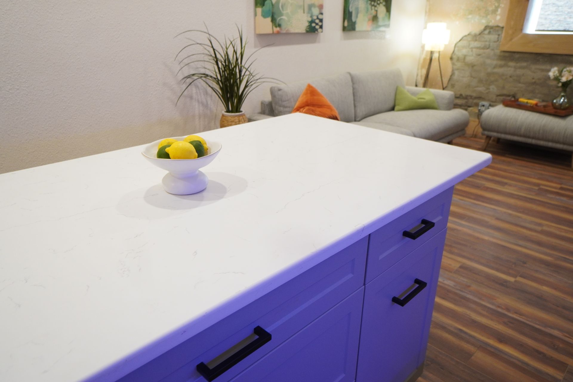 Kitchen island with a white countertop and drawers; bowl of lemons. Living area in background.