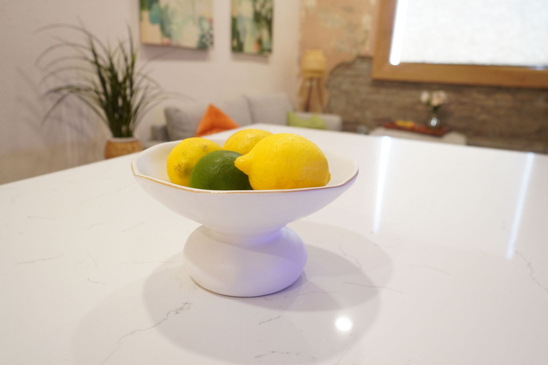 White pedestal bowl of lemons and lime on a white countertop.