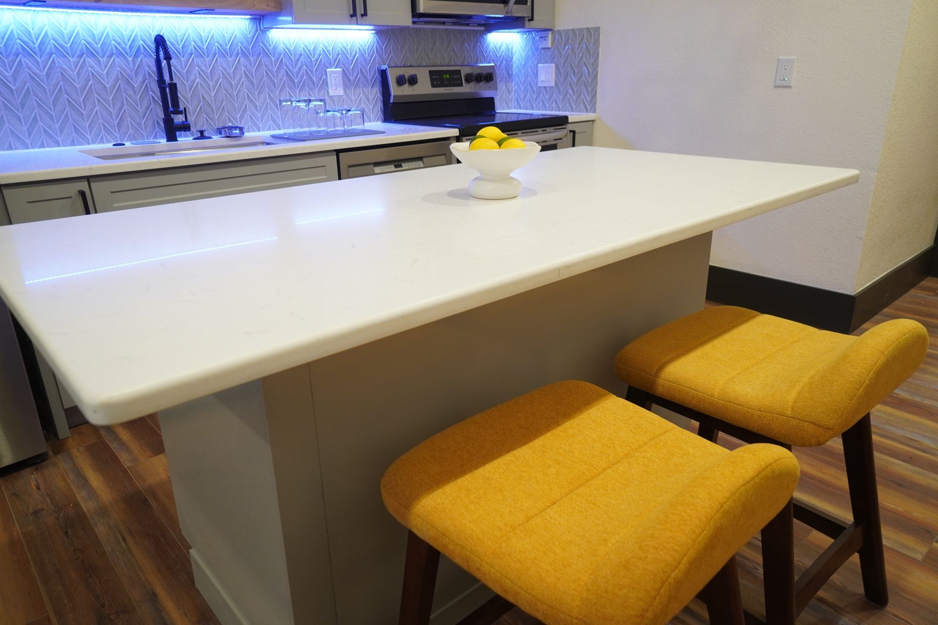 Kitchen with white island, yellow bar stools, and countertop with fruit.