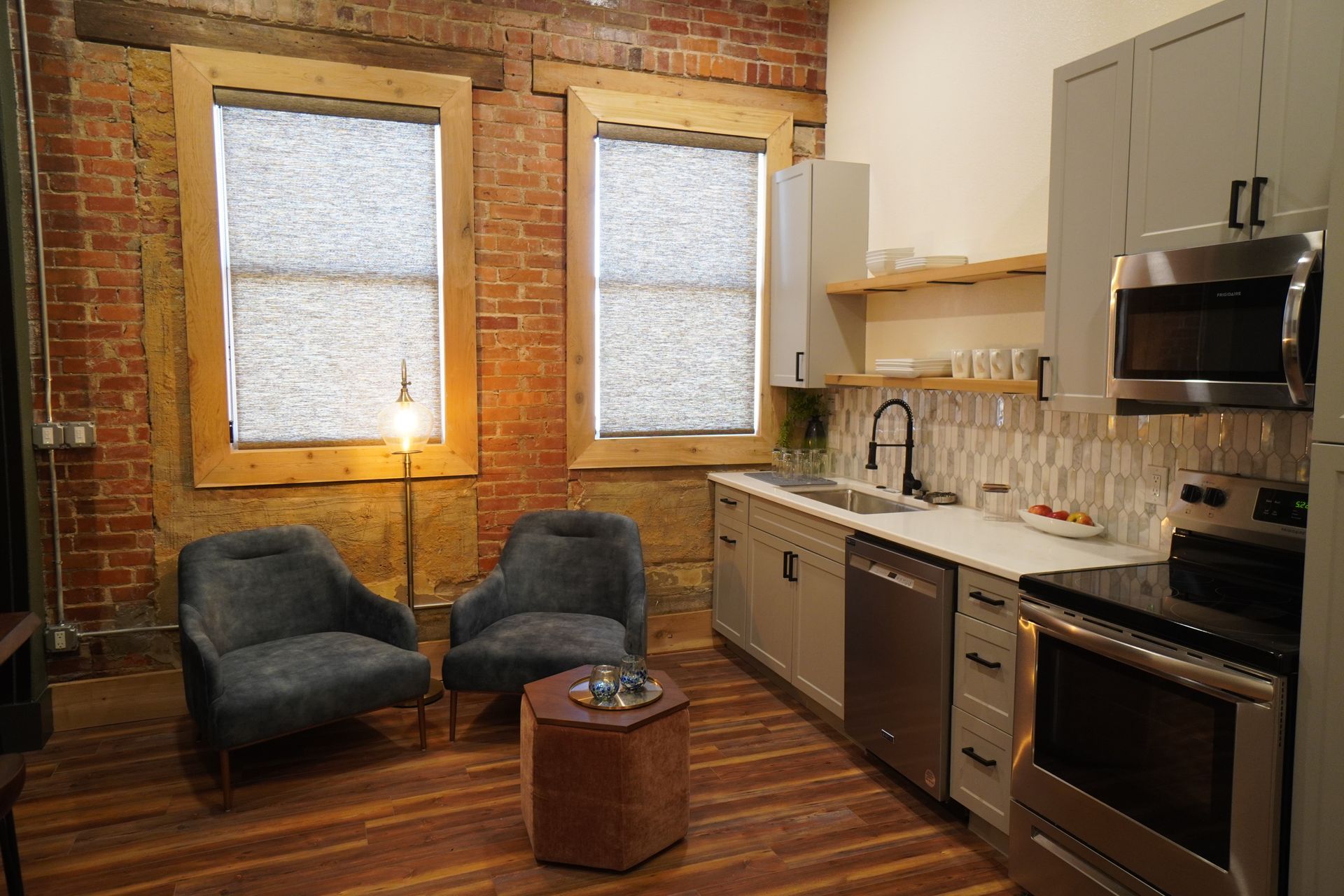 Cozy kitchen with brick wall, gray cabinets, stainless steel appliances, and two armchairs.