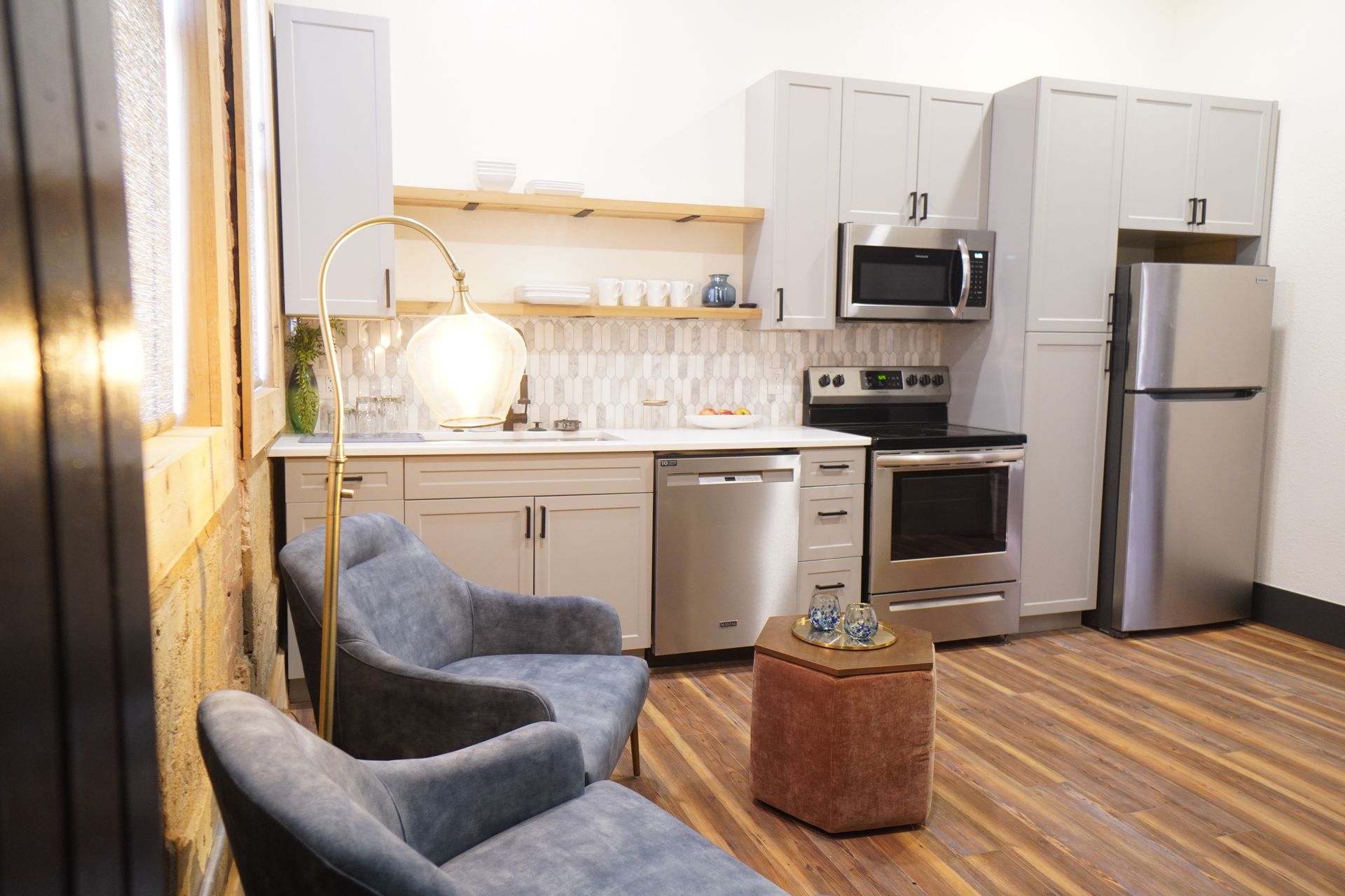 Modern kitchen with gray cabinets, stainless steel appliances, and two blue armchairs.
