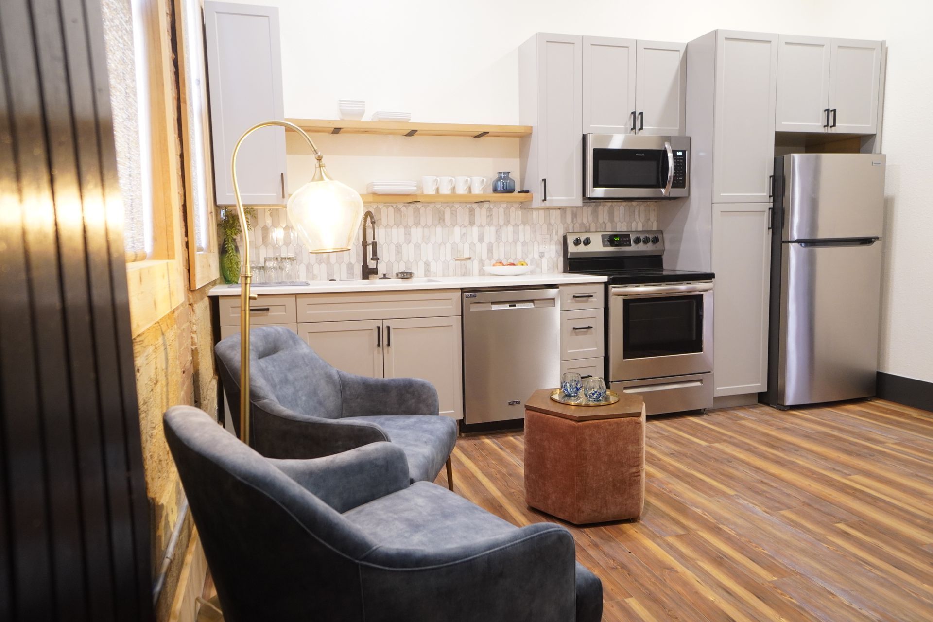 Modern kitchen with gray cabinets, stainless steel appliances, and two blue armchairs.