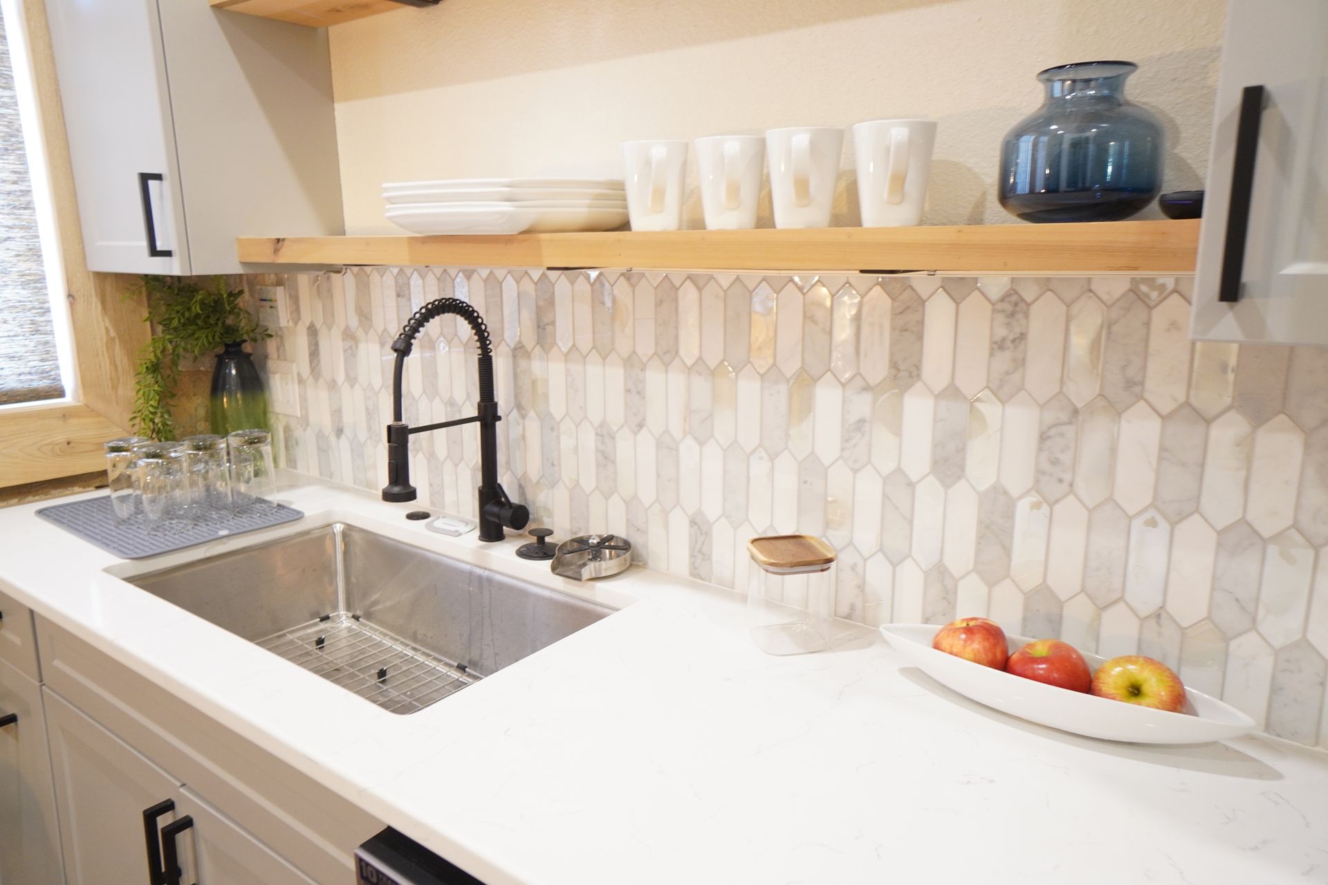 Kitchen with white cabinets, stainless steel sink, black faucet, and patterned backsplash.
