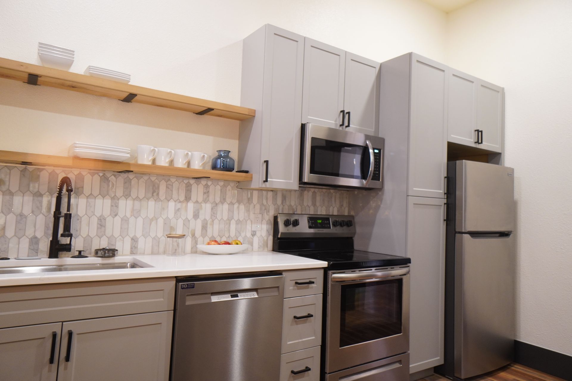 Modern kitchen with gray cabinets, stainless steel appliances, and wood shelves.